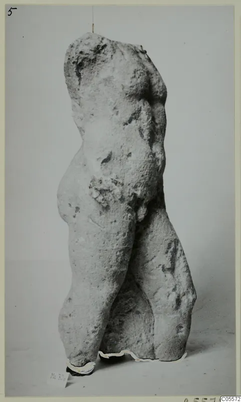 Headless, armless torso of a standing figure in pale stone, from Mersinaki, photographed against a grey backdrop