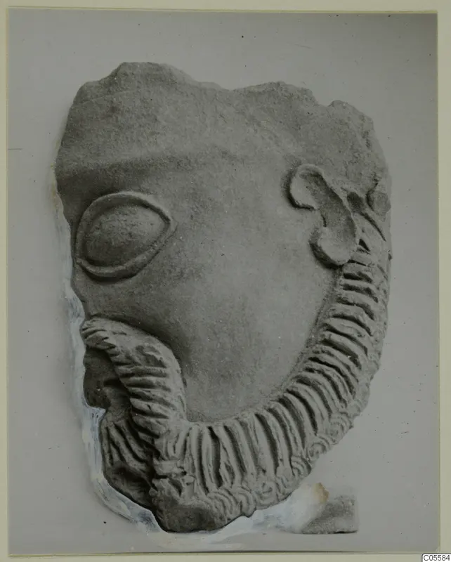Fragment of a carved face from Mersinaki, with an almond-shaped eye, a curled ear and a ridged beard