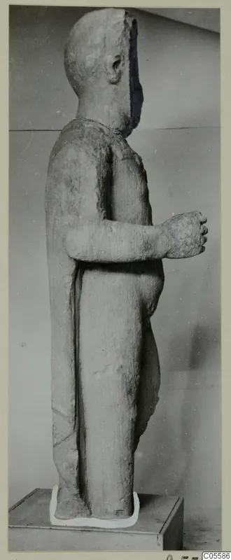 Standing limestone statue of a figure from Mersinaki, shown in side profile against a grey wall