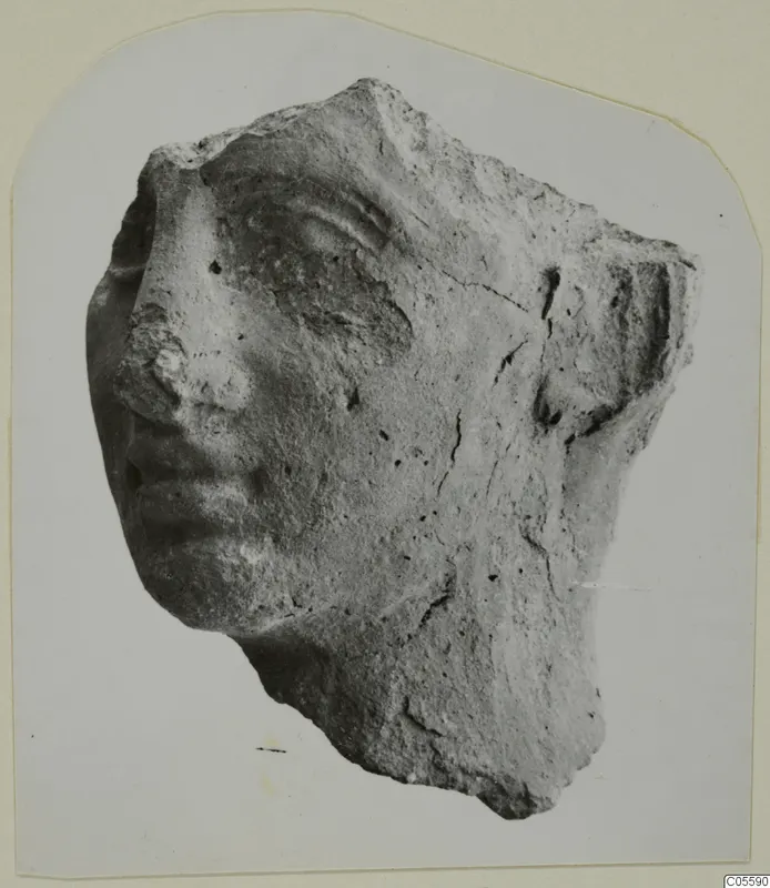 Broken head fragment of a statue, face turned to the left, showing nose, lips and eye.