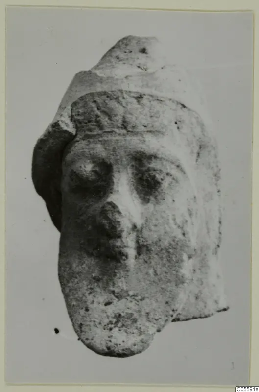 Terracotta head fragment with large eyes, a prominent nose and a band across the brow, shown against a plain background
