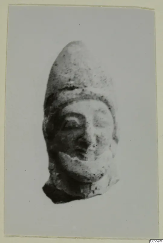 Terracotta head fragment with a tall pointed cap and a broken base, from Mersinaki