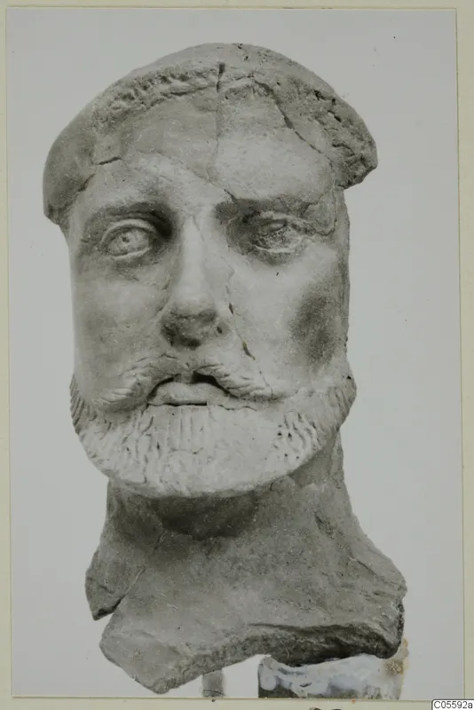Sculpted head of a bearded man in grey terracotta or limestone, shown from the front, with cracks across the face.