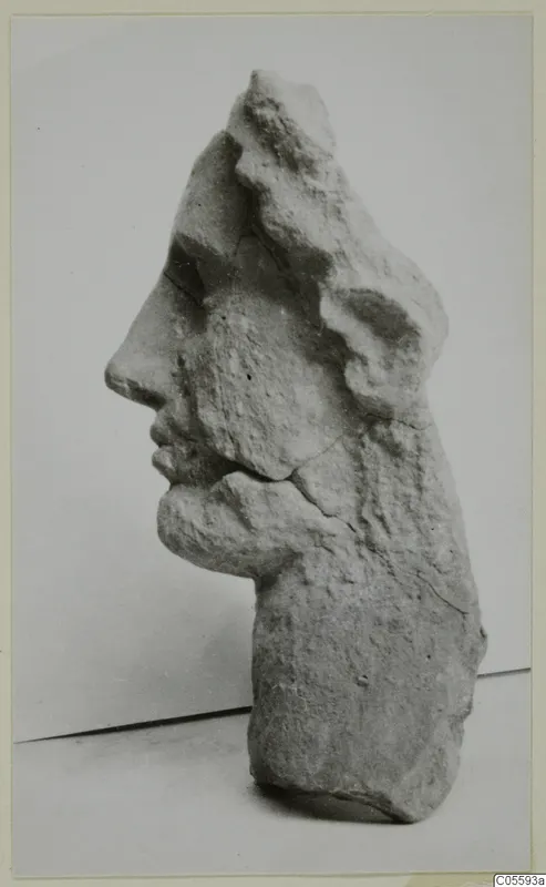 Carved stone head fragment in profile, facing left, with the top and back broken away