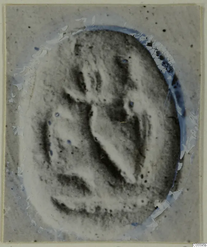 Oval seal or gem with a carved design, photographed on a cracked, damaged mount