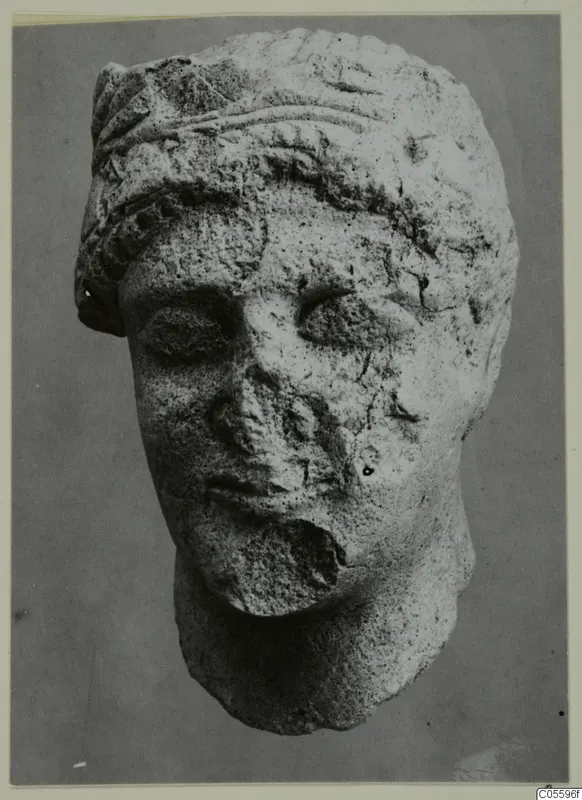 Limestone head sculpture from Mersinaki, shown frontally, with a broken nose and damaged lower face and chin.