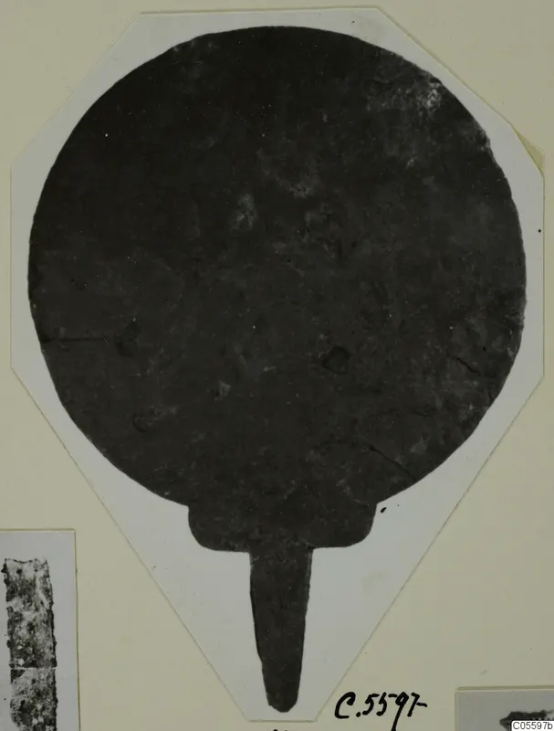 Plate from Marion: a dark round disc with a narrow tang extending downward, shown on a white card mount