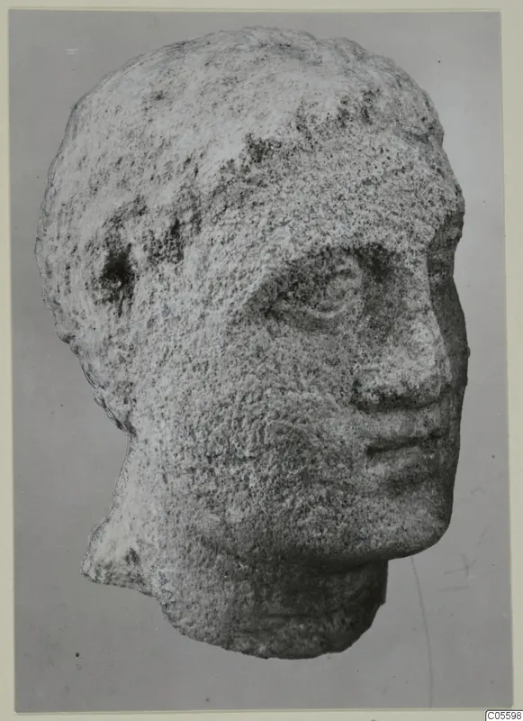 Limestone head statue from Mersinaki, shown in three-quarter view against a grey backdrop.