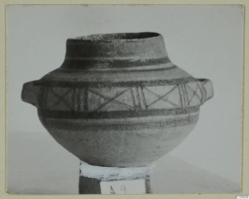 Bichrome IV pottery vessel from Amathus with two side handles and painted bands with cross-hatched panels, photographed on a stand