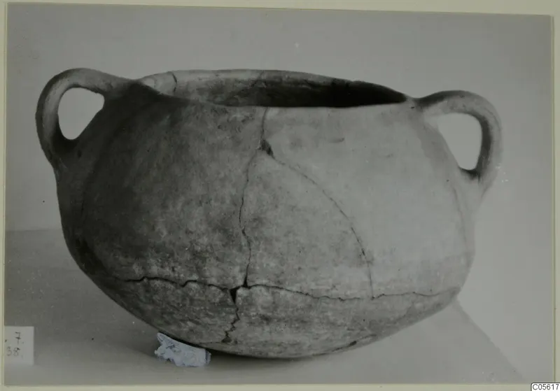 Coarse pottery cooking-pot with two loop handles, photographed on a light surface.