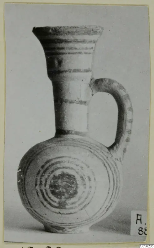White Painted IV juglet with a flared neck, a strap handle and concentric circles painted on the body.