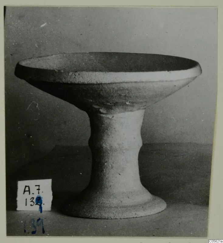 Pale stemmed bowl with a wide shallow bowl and flaring foot, photographed against a grey backdrop