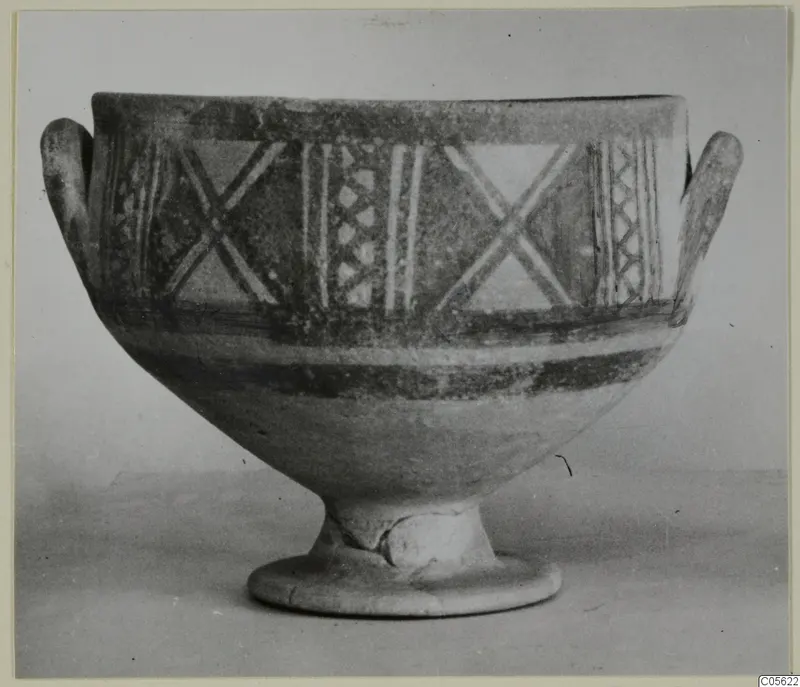 Pottery Bichrome II footed bowl with two side handles, painted with crossed diagonal strokes and vertical bands.
