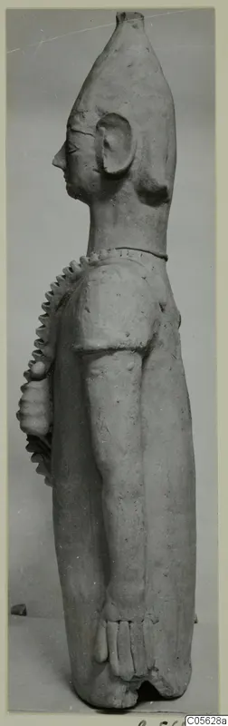 Terracotta standing figure in side view, with a tall head and serrated ridges over the shoulder and chest.