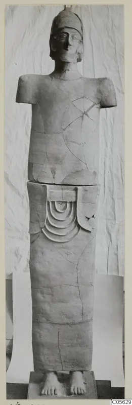 Terracotta statue of a standing figure with a cap-like head and no arms, on a square base.