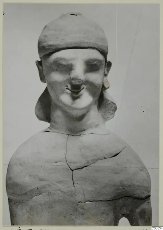 Terracotta Cypro-Greek I statuette of a figure in a close-fitting cap, with large ears and earrings, seen from the front