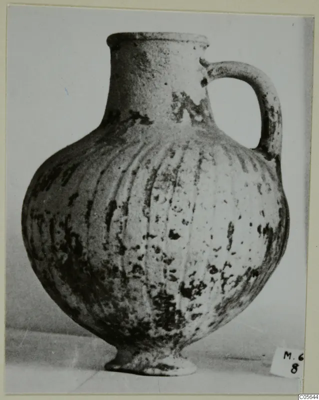 Pottery Black Slip jug with a single loop handle and vertical grooves on its rounded body