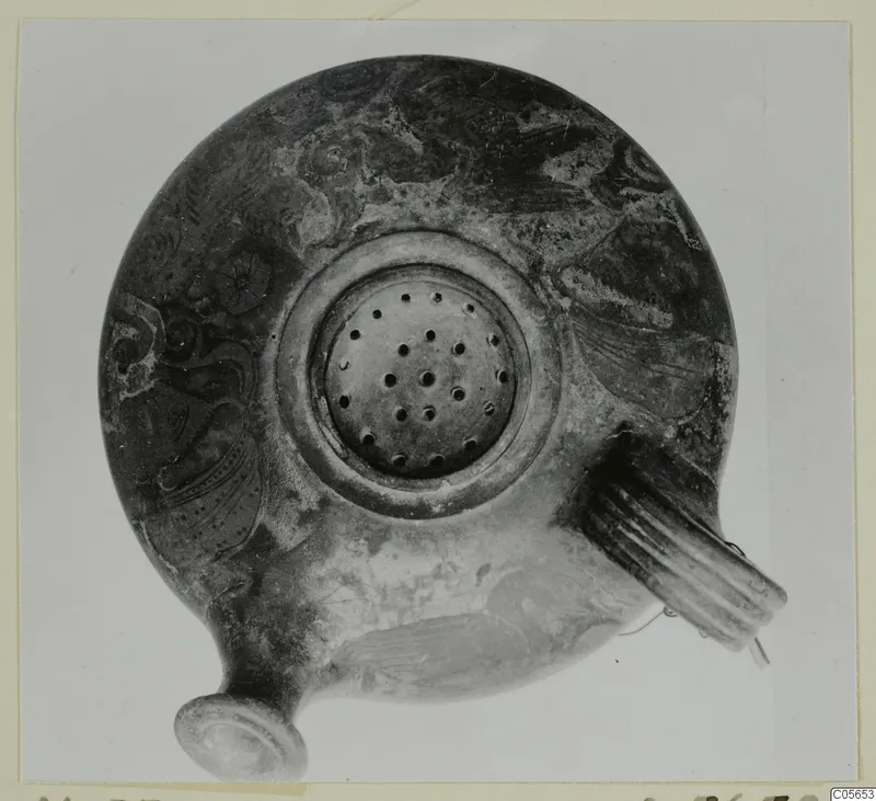 Oil lamp seen from above, with a central filling hole, a ribbed handle on the right and dark painted decoration