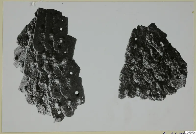 Two corroded iron fragments on a pale background, the larger one made of overlapping plates with small round holes.