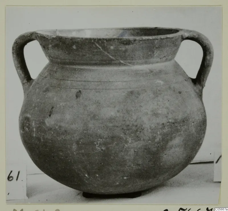 Two-handled vessel with a wide mouth and rounded body, photographed on a light surface with a number label beside it
