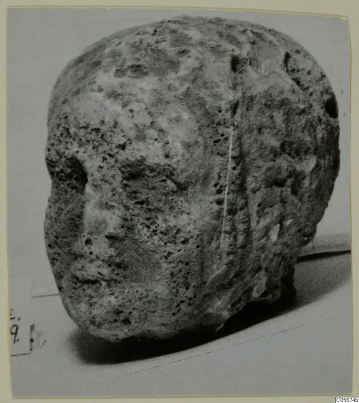 Weathered limestone head fragment from Mersinaki, showing a worn face on its left side with nose and mouth visible