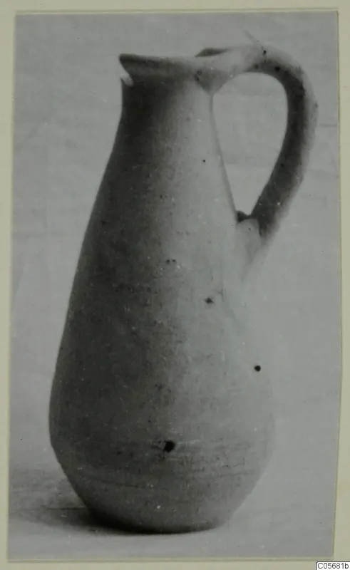 Plain white pottery jug with a tall neck, trefoil-type spout and a single loop handle, photographed on a pale ground.