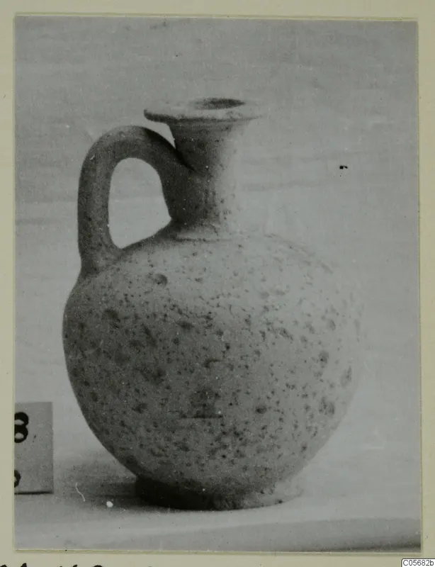Pottery jug with a single loop handle and a flared rim, shown on a plain surface beside a number label.