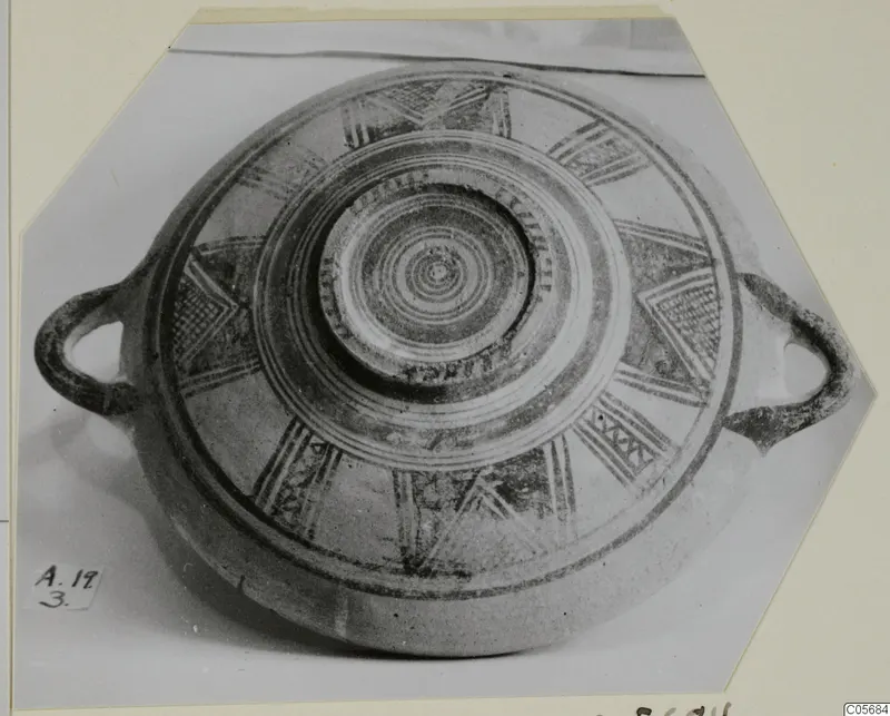 Round pottery vessel with two loop handles, seen from above, decorated with concentric rings and radiating painted motifs.