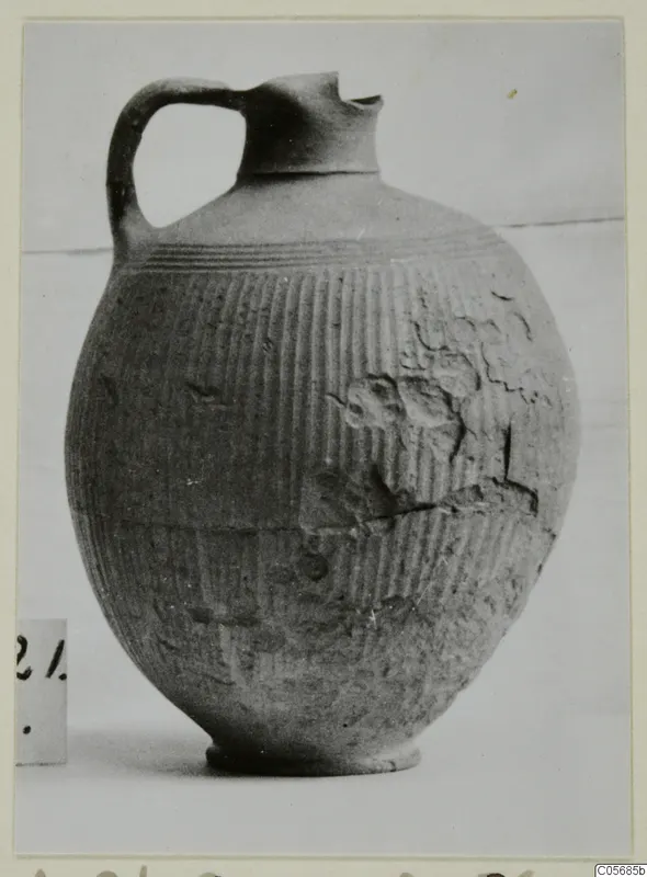 Foreign Red Slip jug with a strap handle, pinched spout and vertically ribbed body
