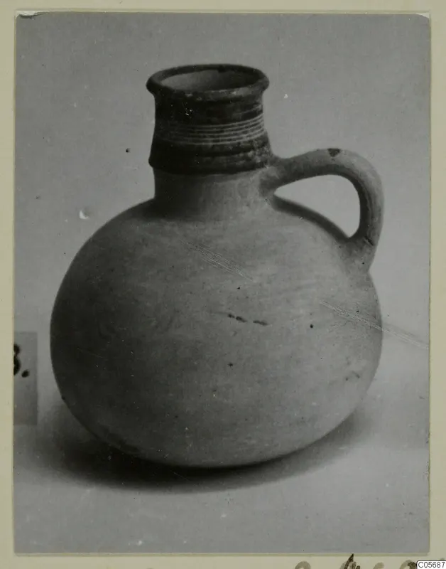 Round jug with a ribbed neck and a strap handle, photographed on a plain grey background. Find from Amathus, tombs 10–26.