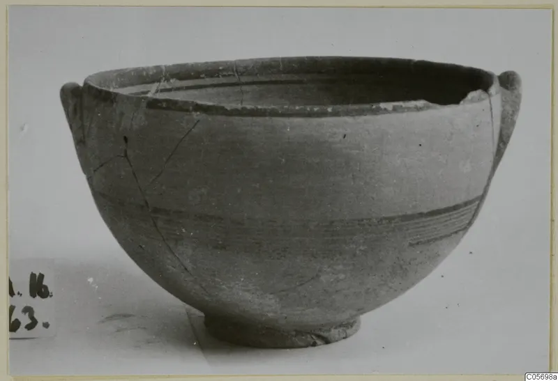 Pottery Black-on-Red bowl with two small handles and dark painted bands on its body, seen from the side.
