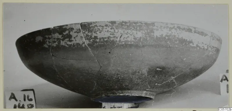 Pottery Red Slip bowl, a shallow bowl with a ring foot, cracked and mended, shown on a dark stand