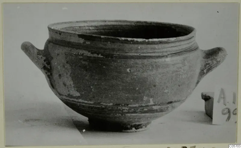 Pottery bowl with two horizontal handles and a wide rim, photographed on a pale surface, from Amathus tombs