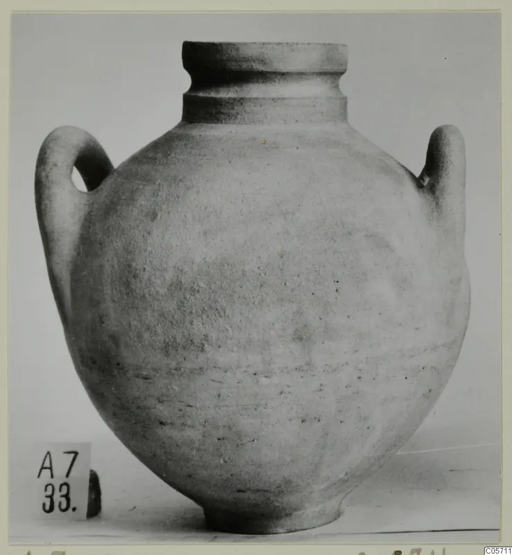 Two-handled jar against a light backdrop, with a number label at its base.