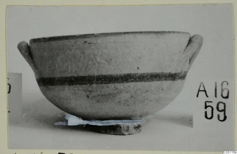 Pottery bowl with two horizontal handles and dark painted bands, photographed on a stand against a grey background.