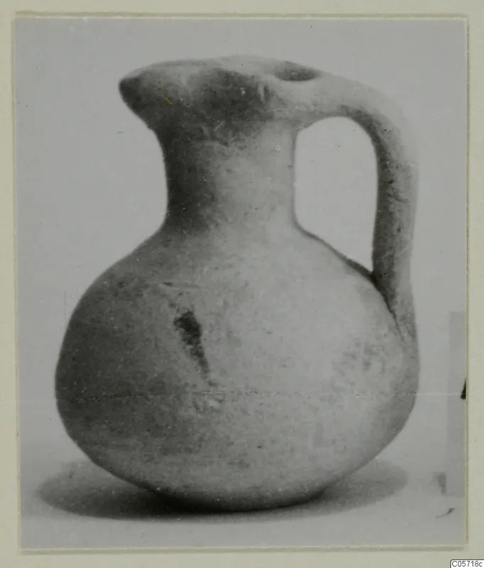 Plain white pottery juglet with a round body, short neck and loop handle, shown against a pale background.