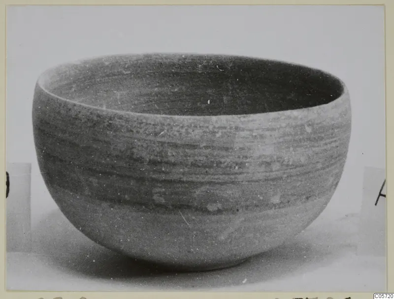 Rounded pottery bowl with horizontal banding, photographed on a plain pale surface