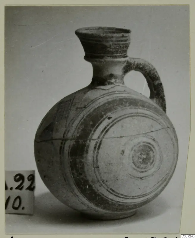 Round-bodied jug with a flaring neck, single loop handle and painted bands, photographed on a plain background