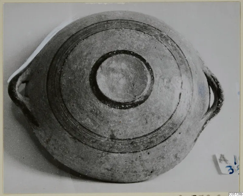 Pottery bowl with two loop handles and concentric dark bands, seen from above against a pale background