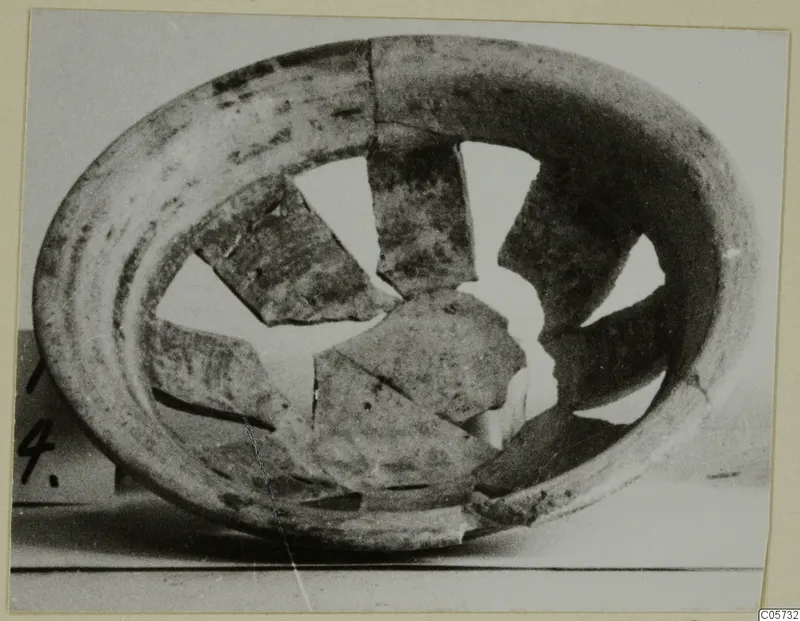 Broken pottery plate-jug seen from above, its rim ring surrounding several missing and displaced wall fragments.