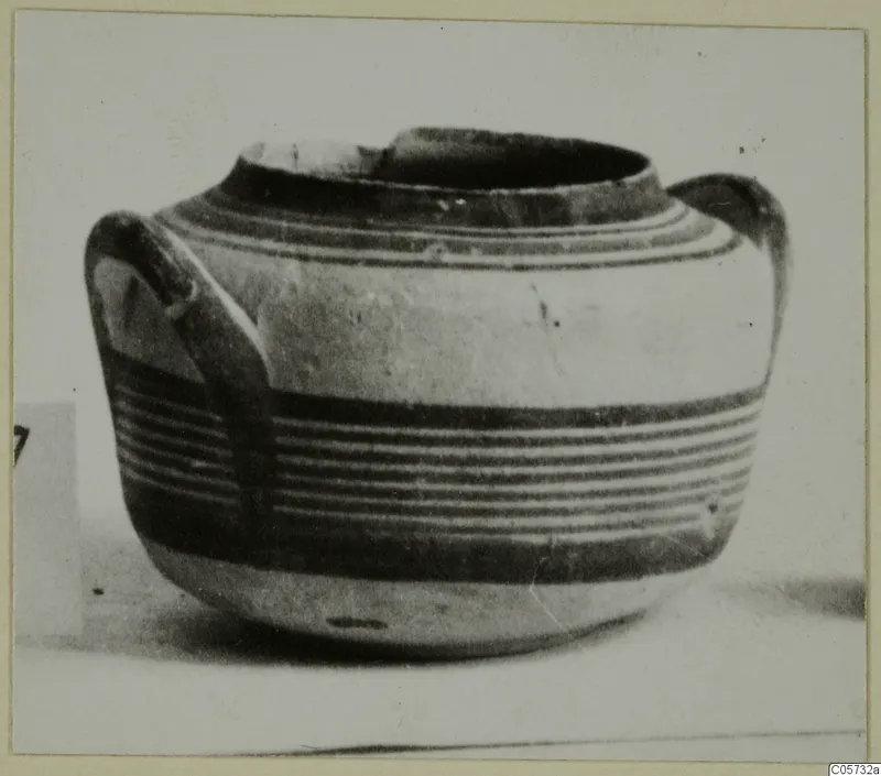 Round-bodied pottery jug with two loop handles and horizontal dark bands, photographed on a plain surface.