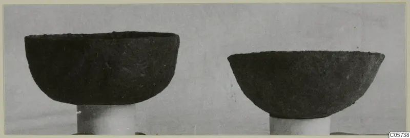 Two dark bowls from Marion Tomb 97, each standing on a white cylindrical support.
