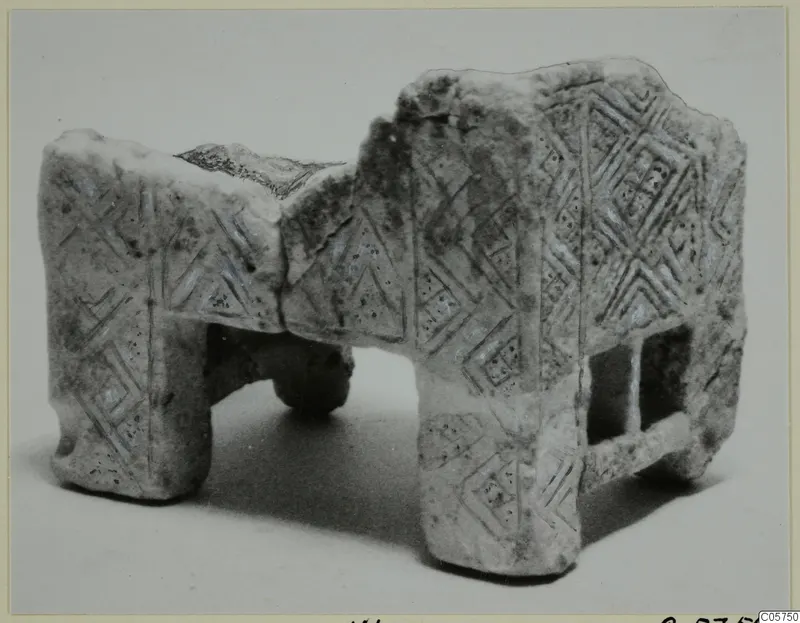 Stone object from Marion with incised lozenge and chevron patterns, standing on four rounded supports.
