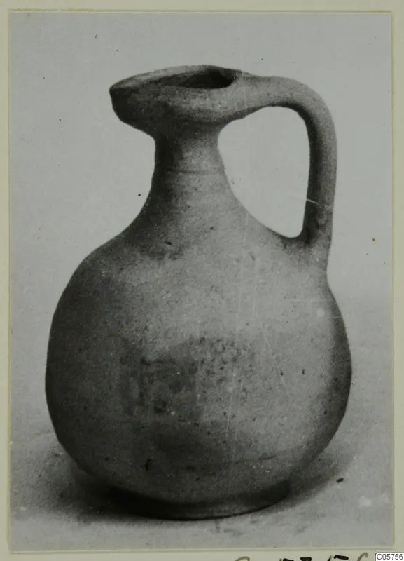 Small pottery jug with a single loop handle and a trefoil-like spout, photographed on a plain surface.