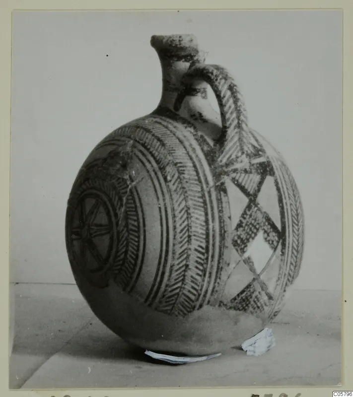 Pottery White Painted I jug with a strap handle, painted with bands, chevrons, a wheel motif and a diamond lattice.