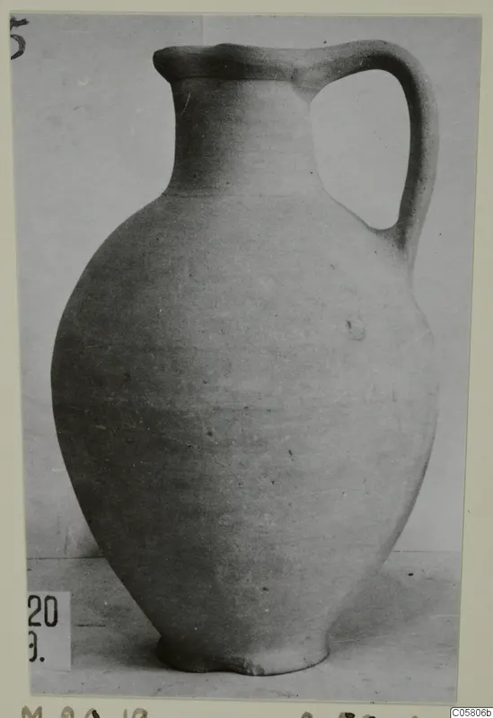 Plain white-slipped pottery jug with a single loop handle, shown against a plain backdrop.
