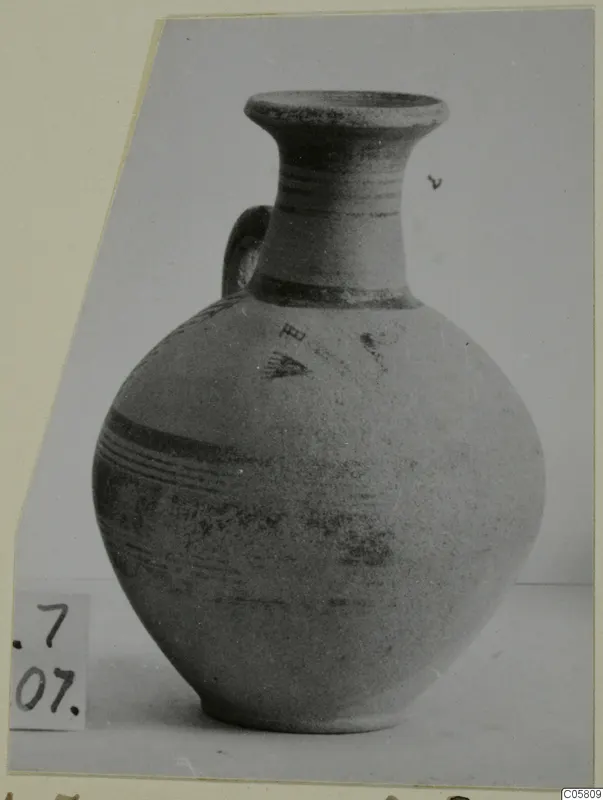 Pottery Bichrome III jug with a flared neck, one handle and painted bands, photographed on a plain surface