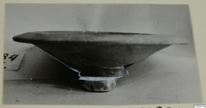 Pottery bowl with a wide flat rim and short foot, seen from the side beside a number label