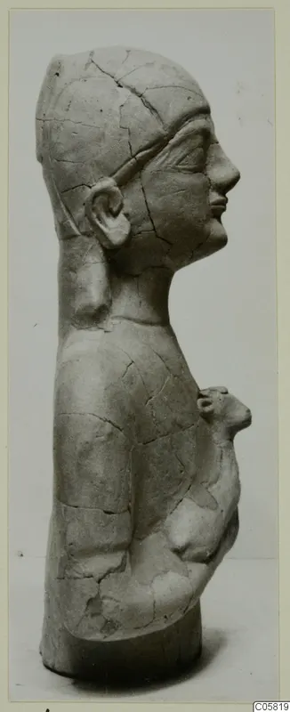 Side view of a cracked pale terracotta statuette of a head and upper body, with a small attached figure at the chest, from Ayia Irini.