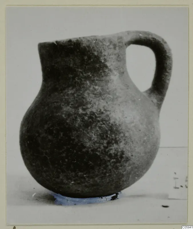 Coarse ware jug with a rounded body, narrow neck and loop handle, photographed on a pale surface.
